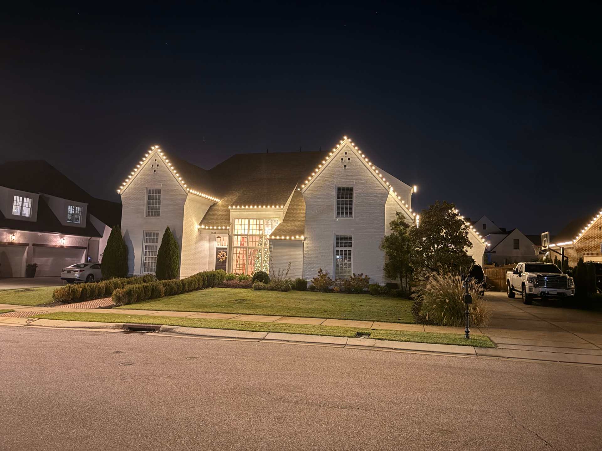 White brick home with warm white Christmas lights outlining the roof